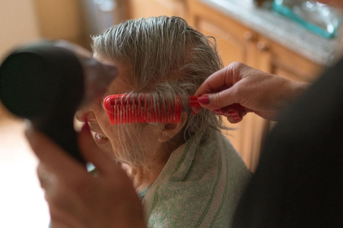 A carer brushing and drying an older woman's hair at home